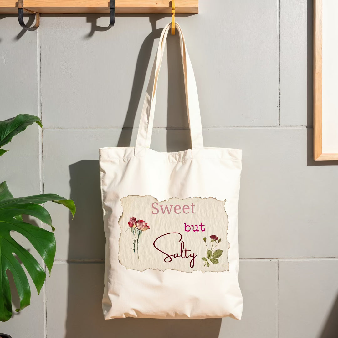 Tote hanging on wall hook with words "sweet but salty" on top of image of vintage paper.