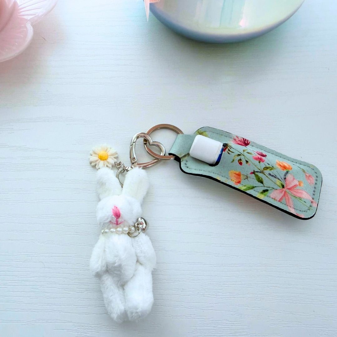 Handmade floral lip balm holder keychain with plush bunny charm, pearl accents, and silver hardware attached to a standard lip balm tube.