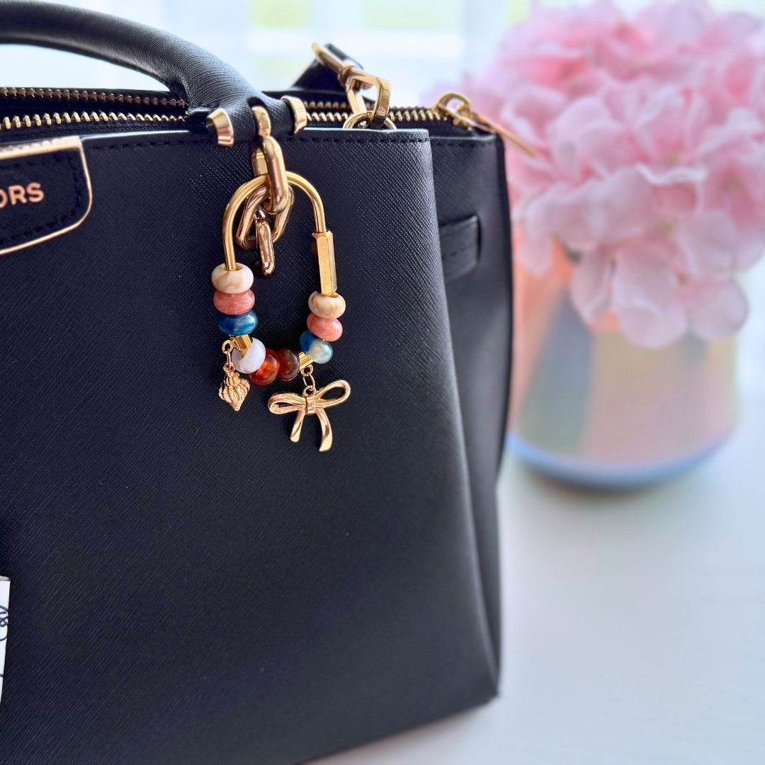 Handmade coastal bow beaded bag charm attached to a black handbag showing the size and everyday styling.