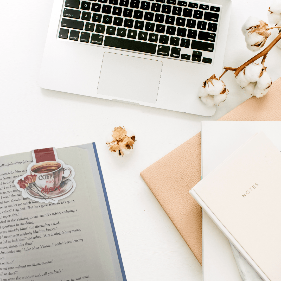 Coffee & Chaos coffee cup magnetic bookmark with floral details styled beside a notebook, laptop, and coffee-themed accessories.
