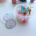 Open DIY bag charm bucket kit with pink silicone beads, bear and flower charms, holographic pouch, and assembly instructions by Splash of Charm.