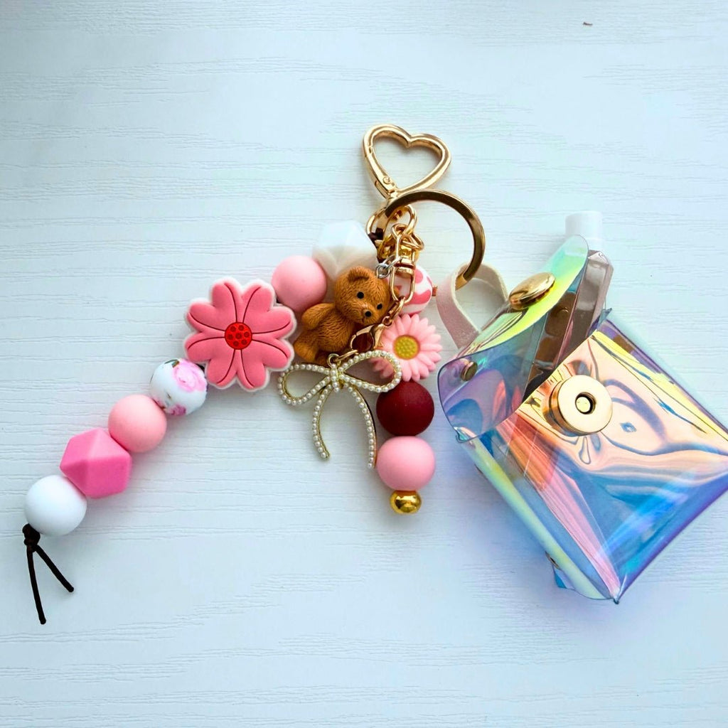 Completed DIY bag charm laid flat with pink floral silicone beads, gold heart clasp, teddy bear accent, and holographic mini pouch.