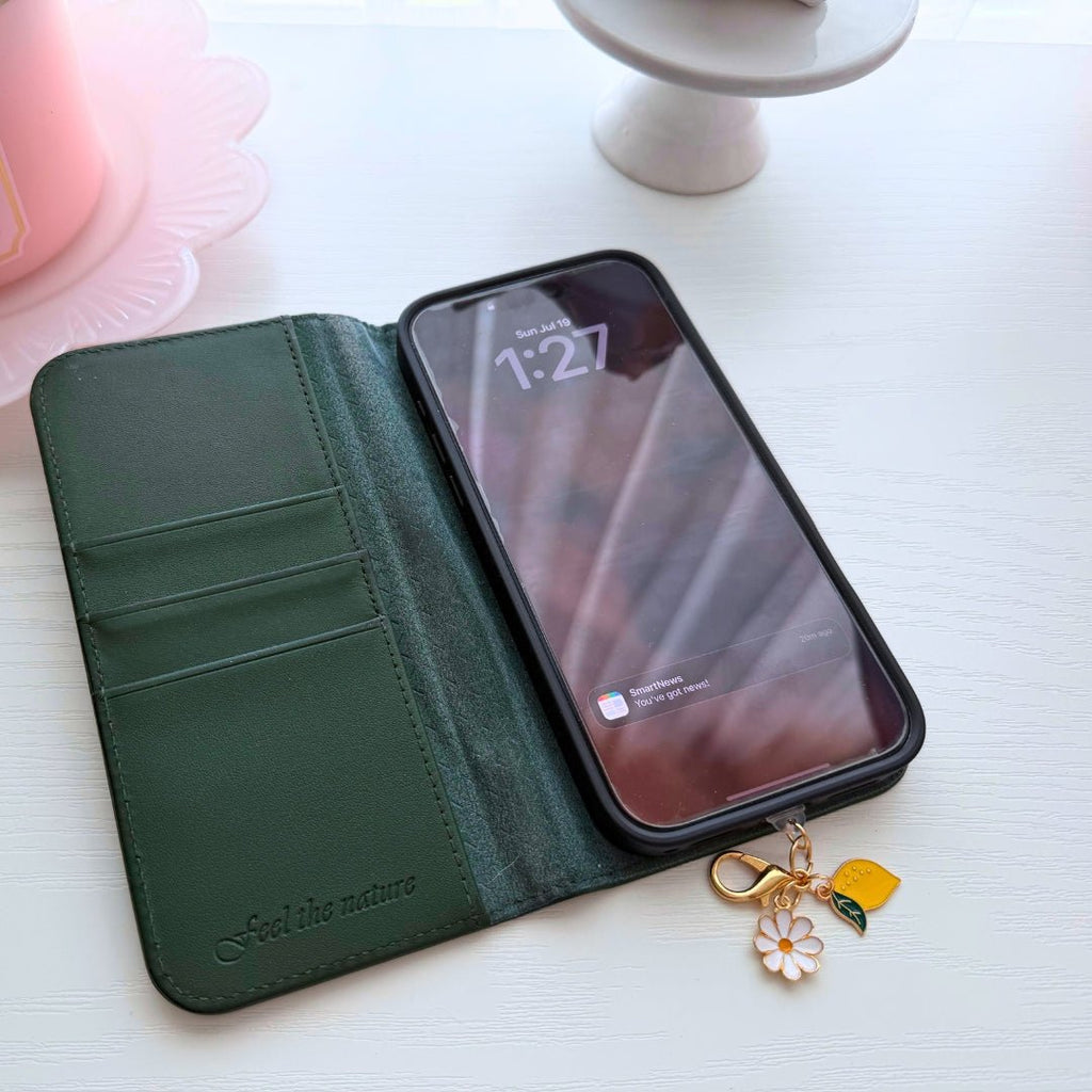 Lemon Daisy phone charm attached to a smartphone in a green wallet case, featuring a gold clasp, white daisy and yellow lemon.