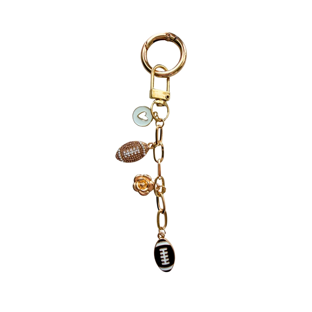 Handmade gold football purse charm with rhinestone football charm, floral charm and black football accent on white background.