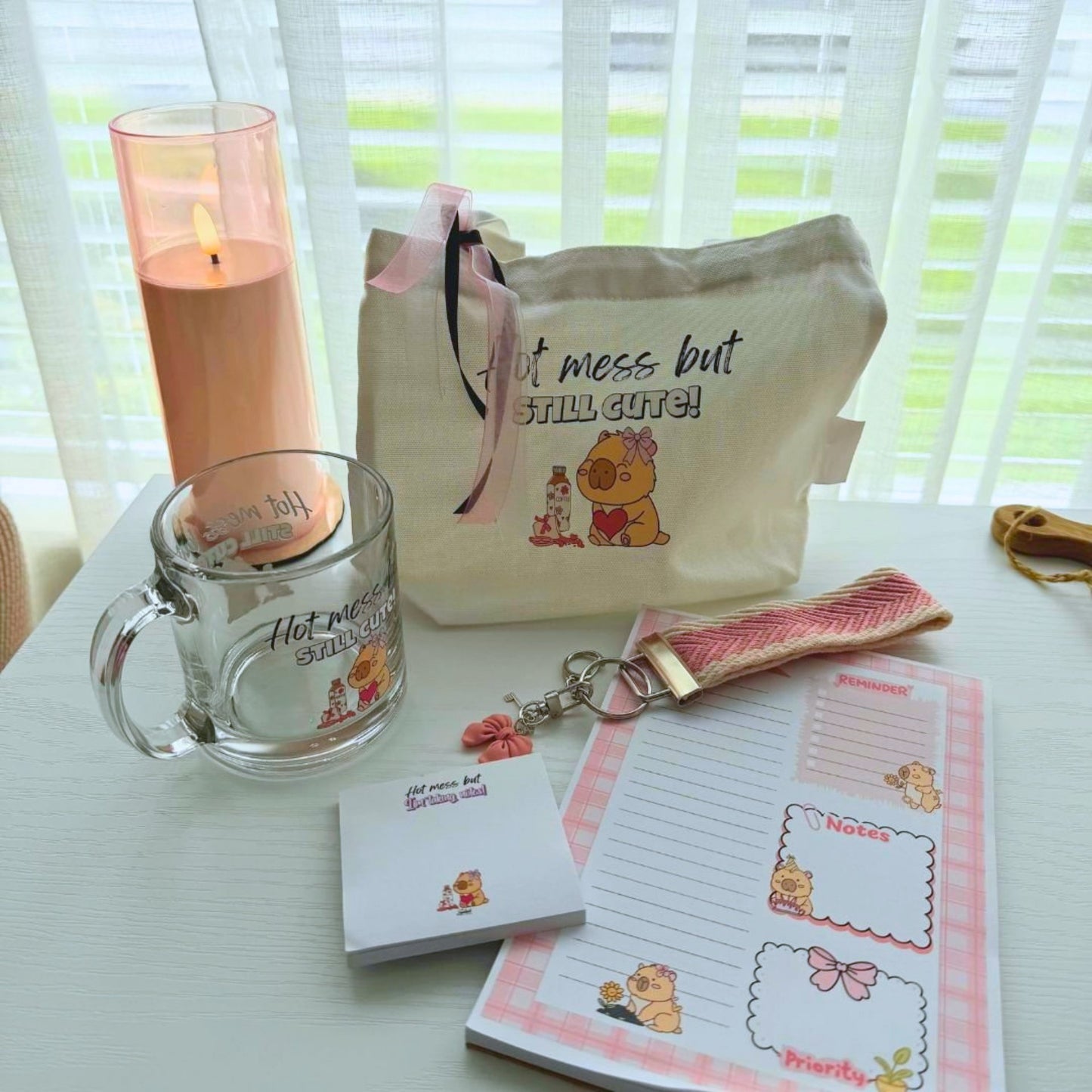 Flat lay of capybara gift bundle showing tote mug notepad sticky notes and charm accessory