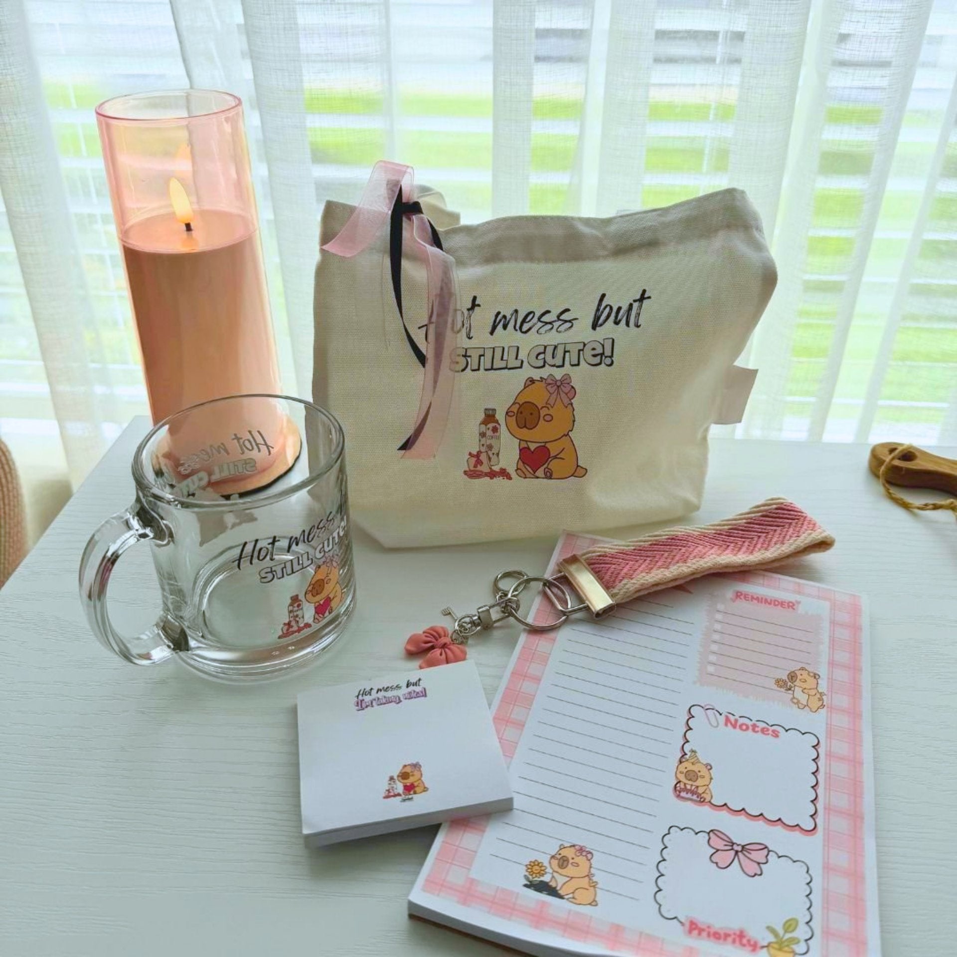 Flat lay of capybara gift bundle showing tote mug notepad sticky notes and charm accessory