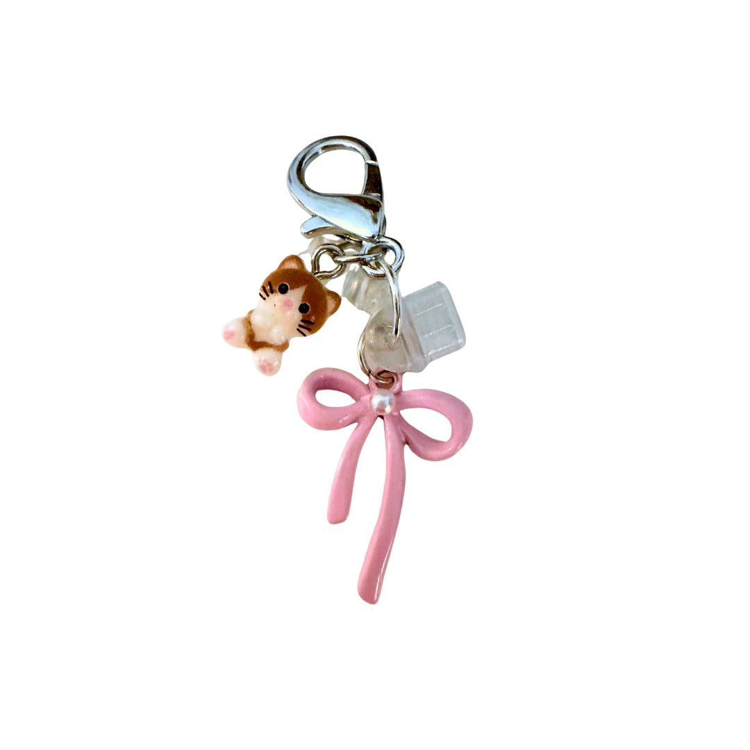 Phone dust cover charm with a brown and white cat, pink bow, clear port covers, and silver-tone lobster clasp