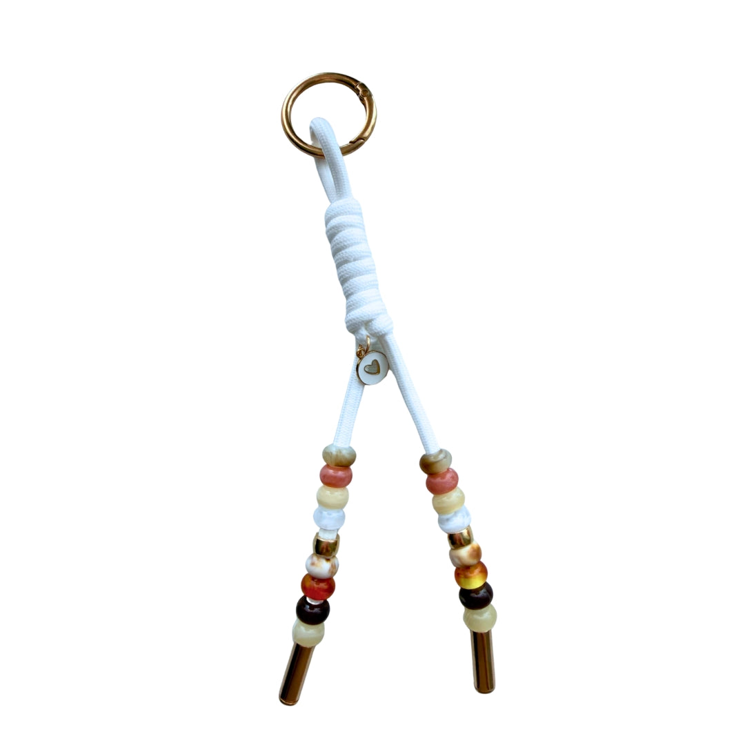 Handmade neutral beaded wristlet purse charm with white cord, gold heart charm, and gold hardware on a white background.