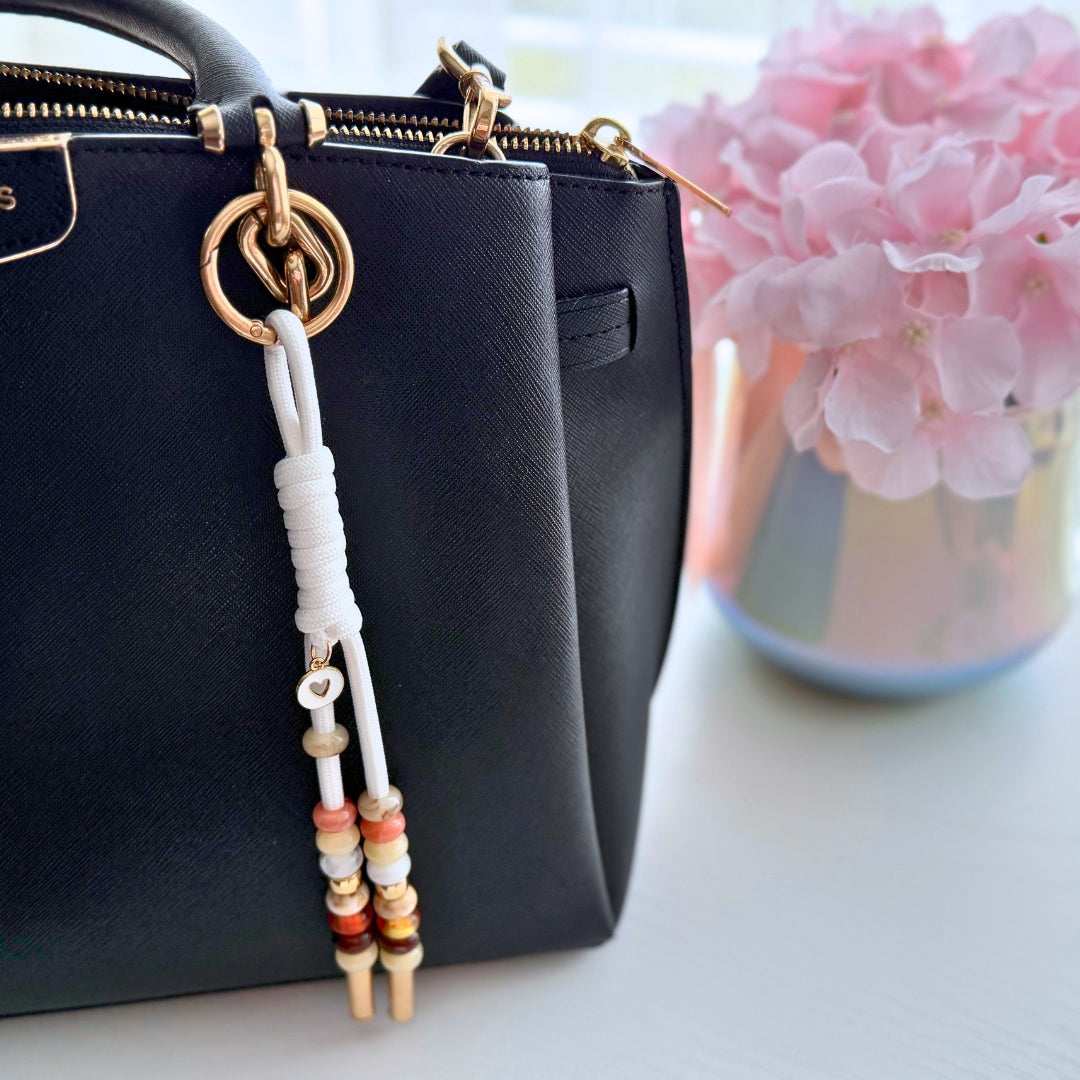 Neutral beaded wristlet purse charm attached to a black handbag showing the size and everyday styling.