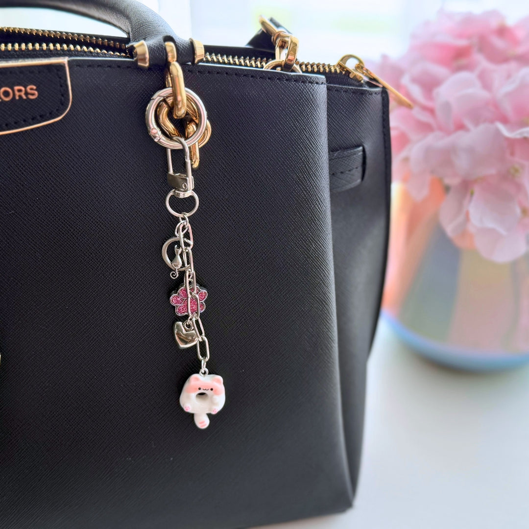 Pink kitty donut purse charm attached to a black handbag showing the size and everyday styling.