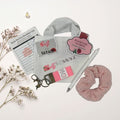White tote bag with branding, pink scrunchie, pen, and other items on a lace doily.