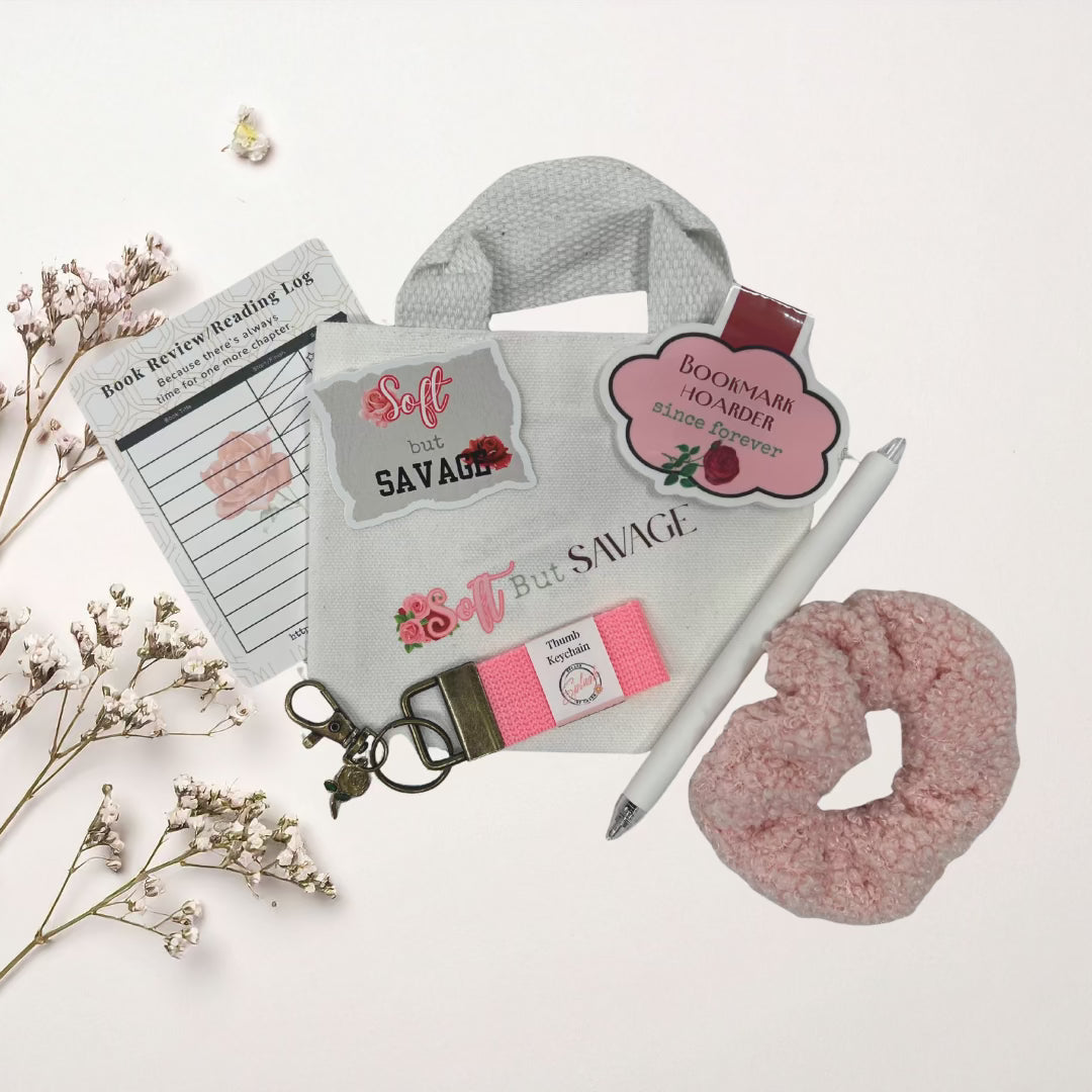 White tote bag with branding, pink scrunchie, pen, and other items on a lace doily.